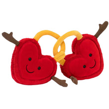 Two plush toy hearts in red with yellow accents, connected by a golden cocoa-shaped ring, with smiling faces and arms extended.