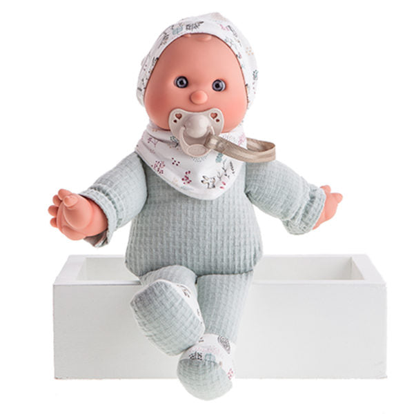 A baby doll with a pacifier, wearing a grey outfit and a hat, sitting in a white box.