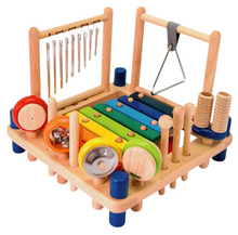 A wooden musical instrument toy set for children, featuring a variety of colorful instruments including a xylophone, drum, chimes, triangle, cymbal, bells, maracas, castanet, double guiro, and rhythm sticks, with two strikers and one scraper.
