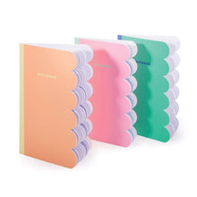 A set of three scalloped edge notebooks in orange, pink, and green colors with a lined pattern on the cover.