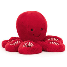 A large red plush toy resembling an octopus with a happy facial expression, featuring a huggable body and cozy, springy arms with candy cane stripes.