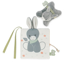 A soft book with a plush donkey design, featuring a gray donkey with a green bow on a white background, accompanied by a small gray stuffed animal on the side.