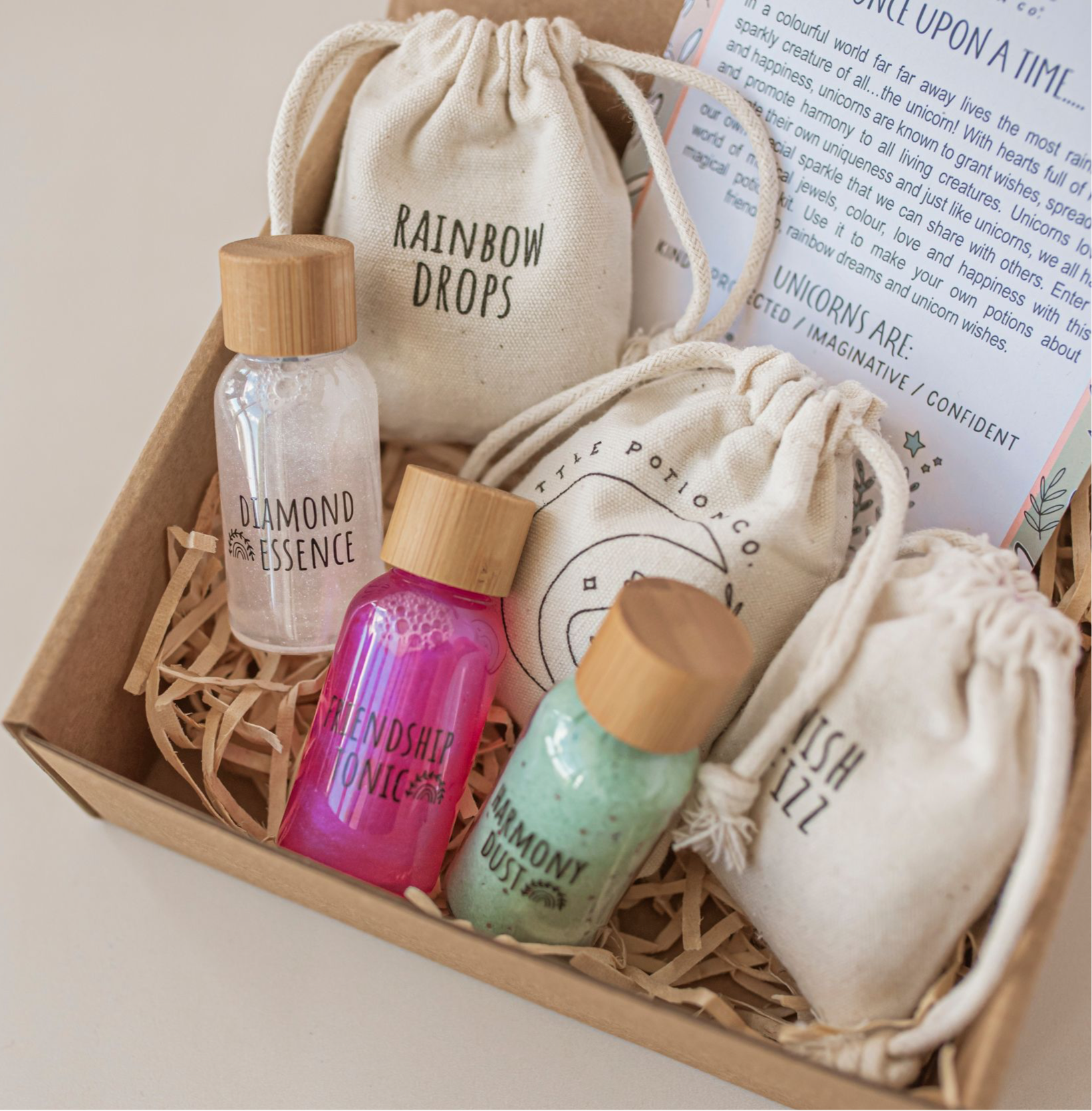 A potion play set designed for children, featuring reusable PET plastic bottles with bamboo screw caps, labeled with different potion names such as Rainbow Drops and Unicorn Tears. The set includes dry ingredients in cotton pouches and a spell card, all presented in a box with a fairy tale theme.