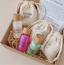 A potion play set designed for children, featuring reusable PET plastic bottles with bamboo screw caps, labeled with different potion names such as Rainbow Drops and Unicorn Tears. The set includes dry ingredients in cotton pouches and a spell card, all presented in a box with a fairy tale theme.