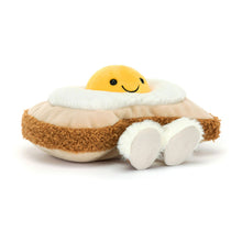 A plush toy resembling an egg with a smiling face on top, sitting on a slice of toast with a textured crust.