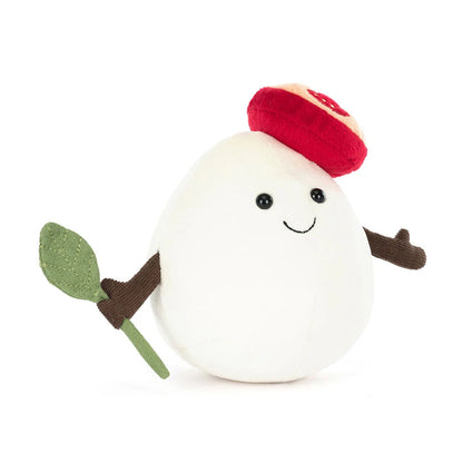 Plush toy resembling a mozzarella cheese ball with a red hat and green leaf, on a white background