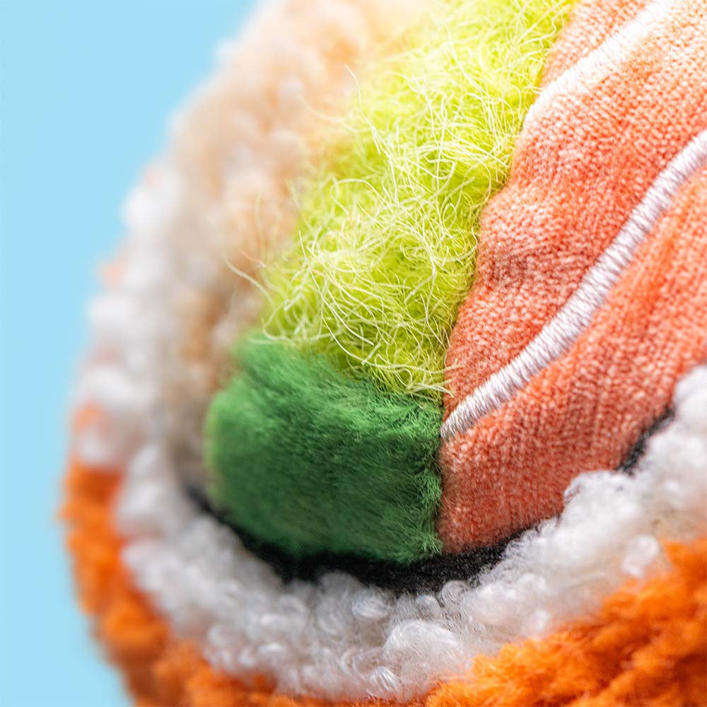Close-up of a colorful fabric ball with green, orange, and white patterns on a light blue background.