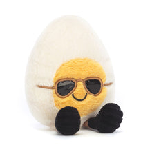 A plush toy resembling a chic egg with soft fur in cream and yellow, wearing sunglasses and black shoes with grey laces.