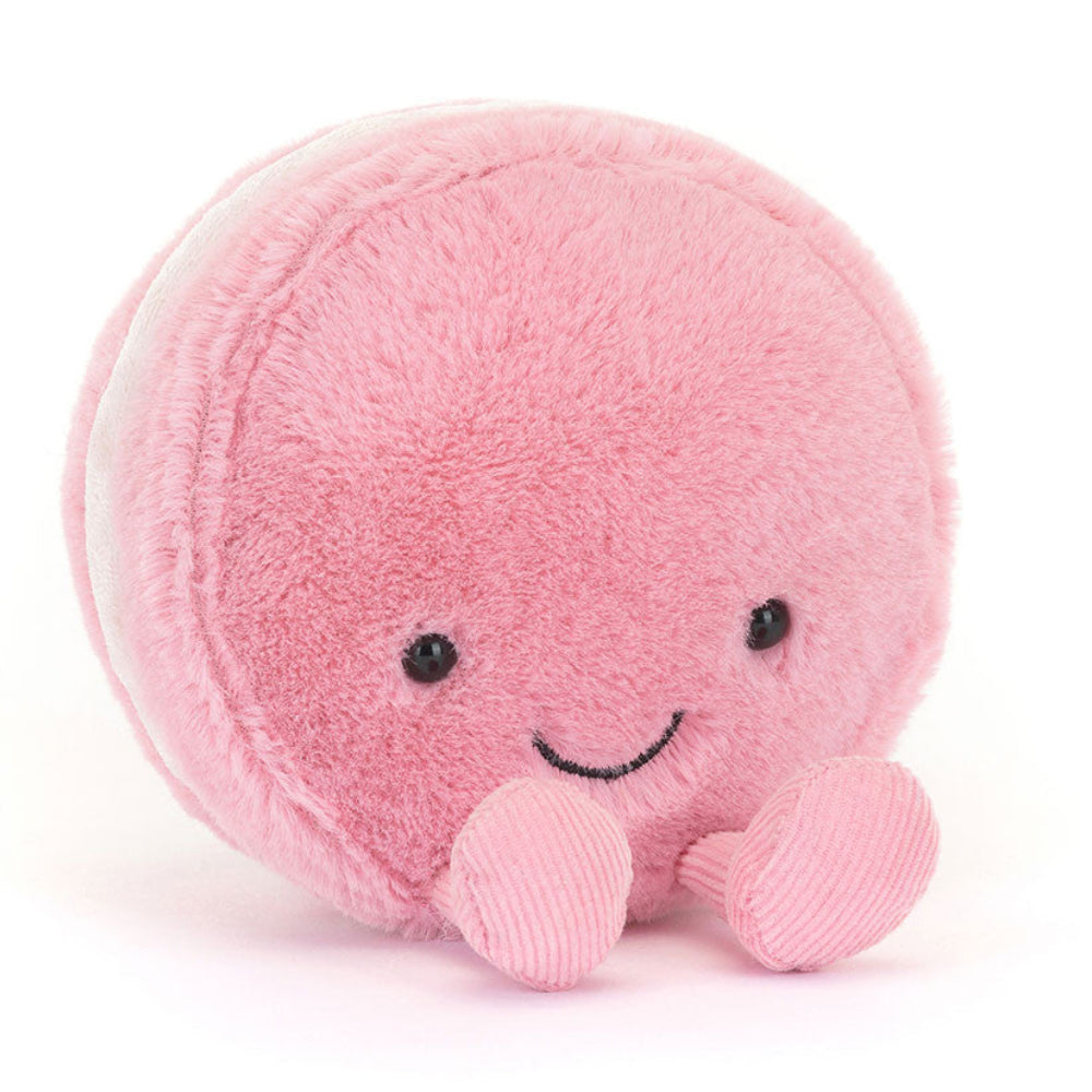 Pink plush macaroon toy with a smiling face on a white background