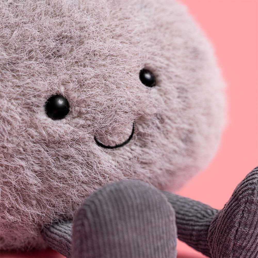 Plush toy resembling a round grey pebble with a smiling face on a pink background