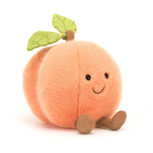 A plush toy resembling a peach with a smiling face, halved and showing the inside with a green leaf on top.