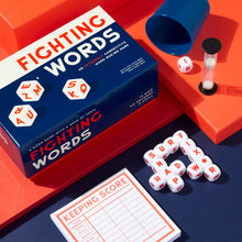 The image shows a game called 'Fighting Words' with dice cups, dice, and a score pad on a table with a bright orange and blue background.