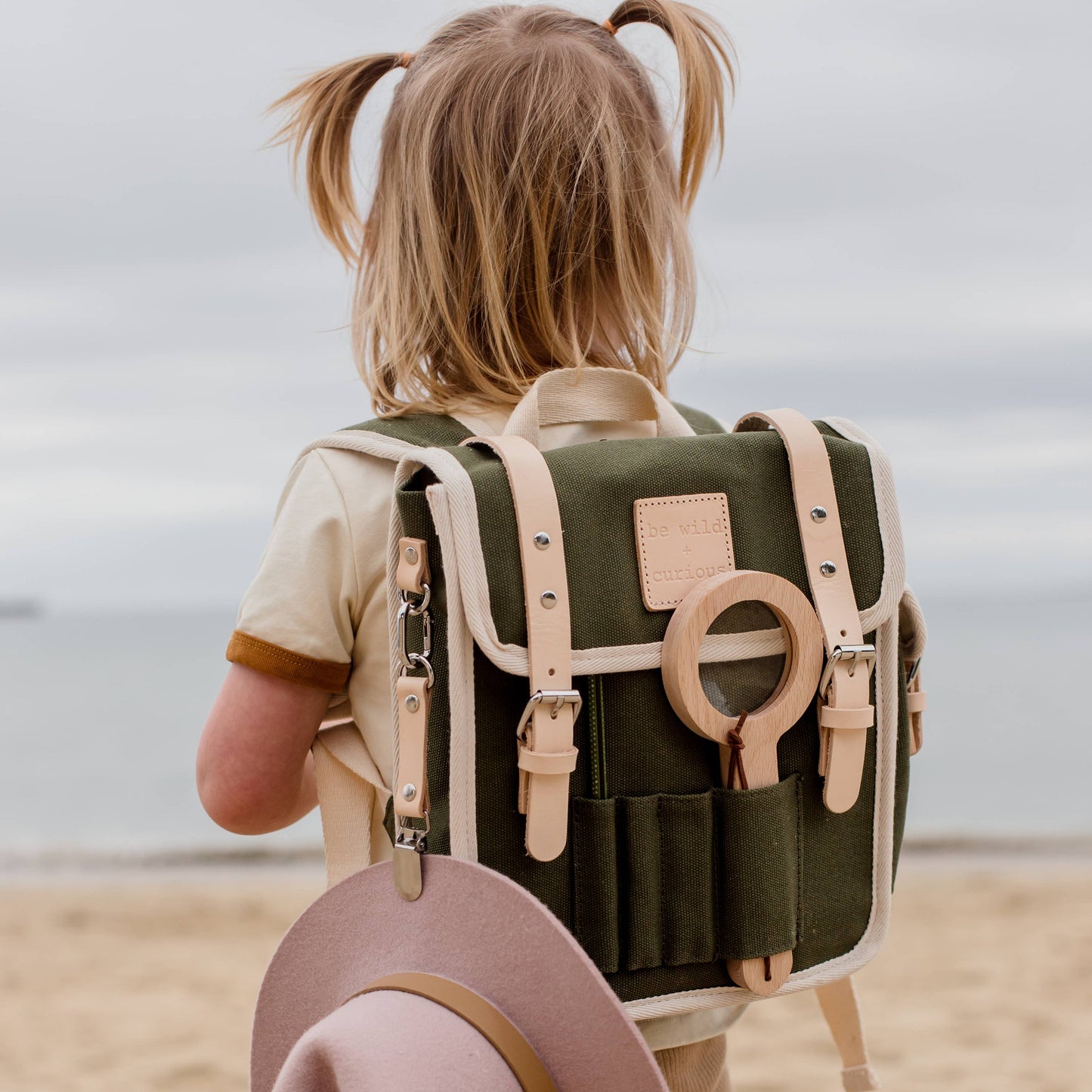 Child with a green backpack and pink hat on a beach