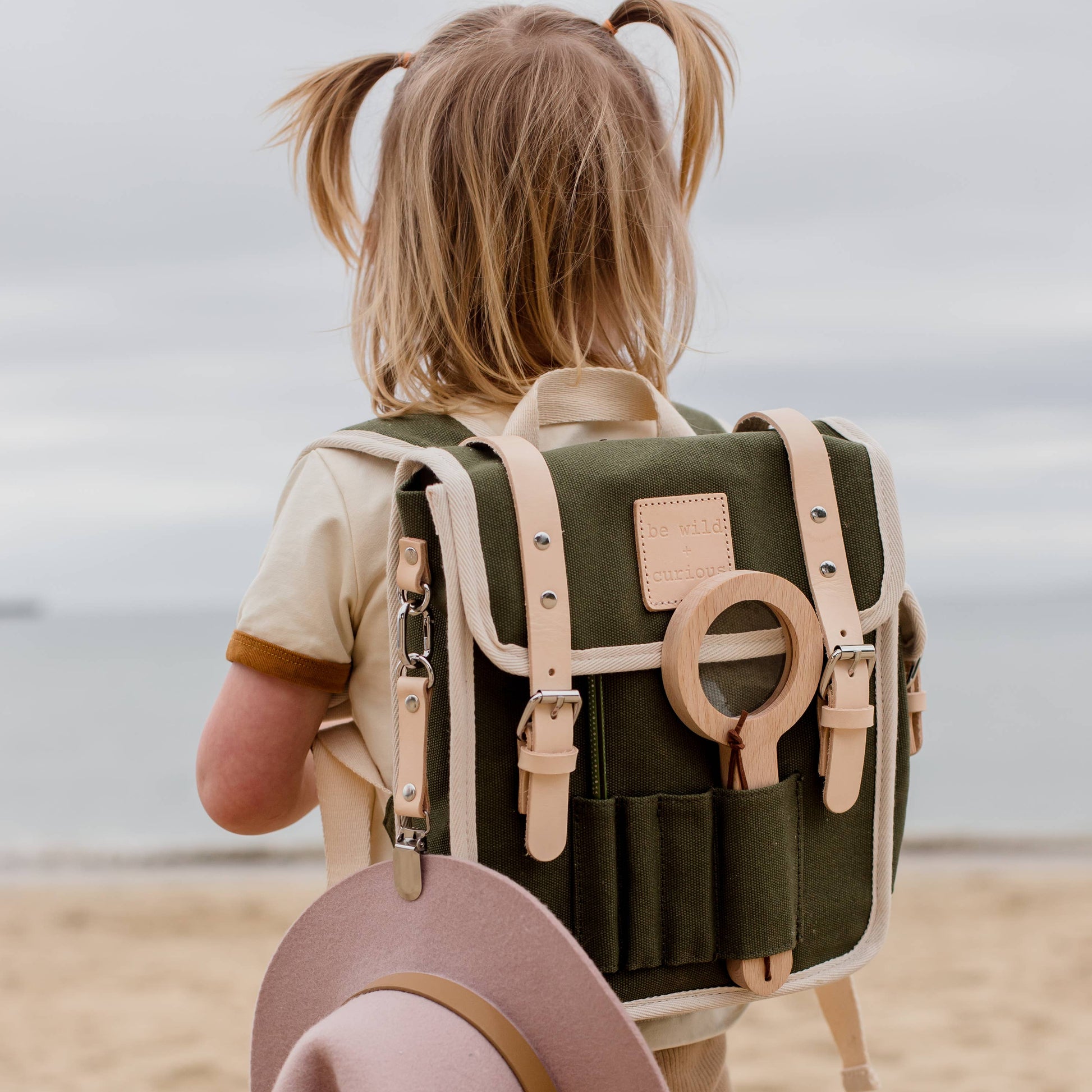 Child with a green backpack and pink hat on a beach