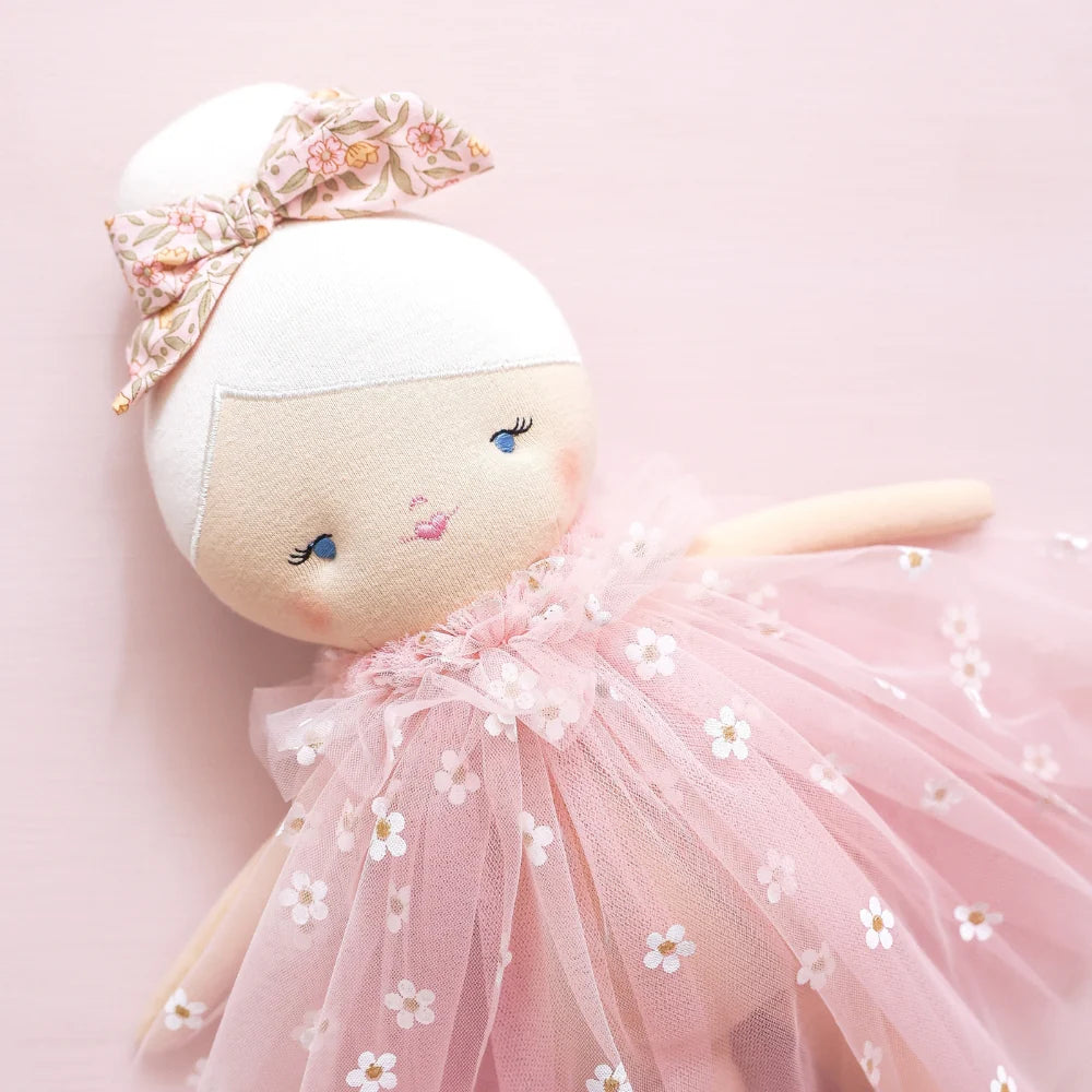 Stuffed doll in a pink tutu with floral headband on a light pink background