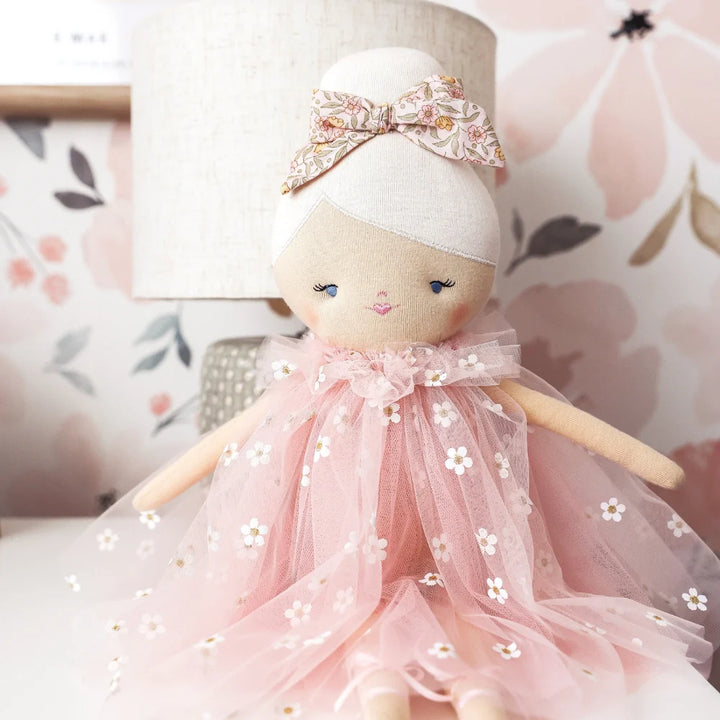 Doll with a pink dress and white headband against a floral background