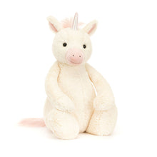 A large plush toy unicorn with soft vanilla fur, pink inner ears and a multicolored horn, seated against a white background.