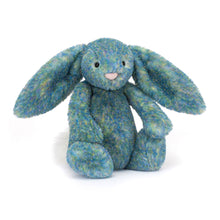 A plush toy bunny with blue, green, and pink fur, featuring long fold ears and a cream bobtail. It has a soft texture and a Jellycat brand tag.
