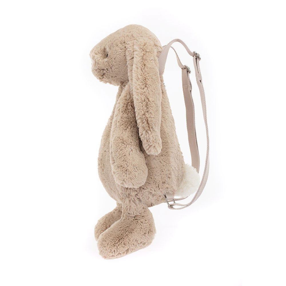 A beige plush backpack designed to look like a bunny with wide adjustable straps and a zip closure. Backpack is Jellycat brand.