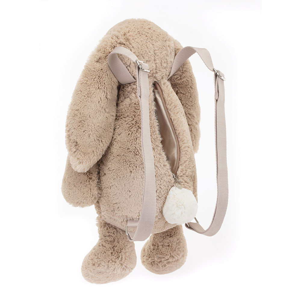 A beige plush backpack designed to look like a bunny with wide adjustable straps and a zip closure. Backpack is Jellycat brand.