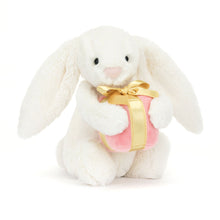A plush toy of a cream-colored bunny with floppy ears, a pink suedette nose, and a pink present with a gold satin bow.