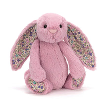 A small pink stuffed bunny with floral fabric details on its ears and feet.