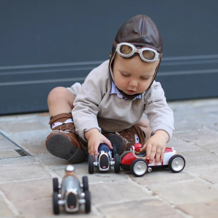 Child playing with toy cars wearing a pilot costume outdoors.