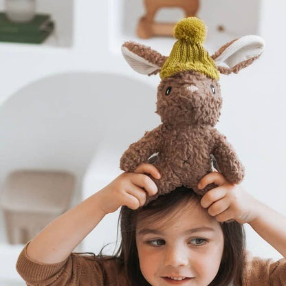 Child wearing a plush toy on their head with a blurred indoor background