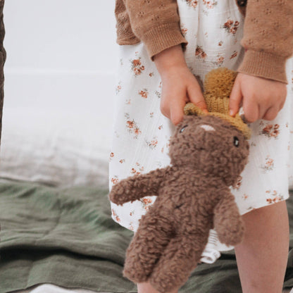 Child holding a brown teddy bear with a patterned dress and sweater
