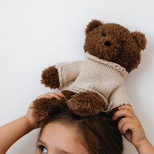 Child wearing a teddy bear plush toy on their head against a white background