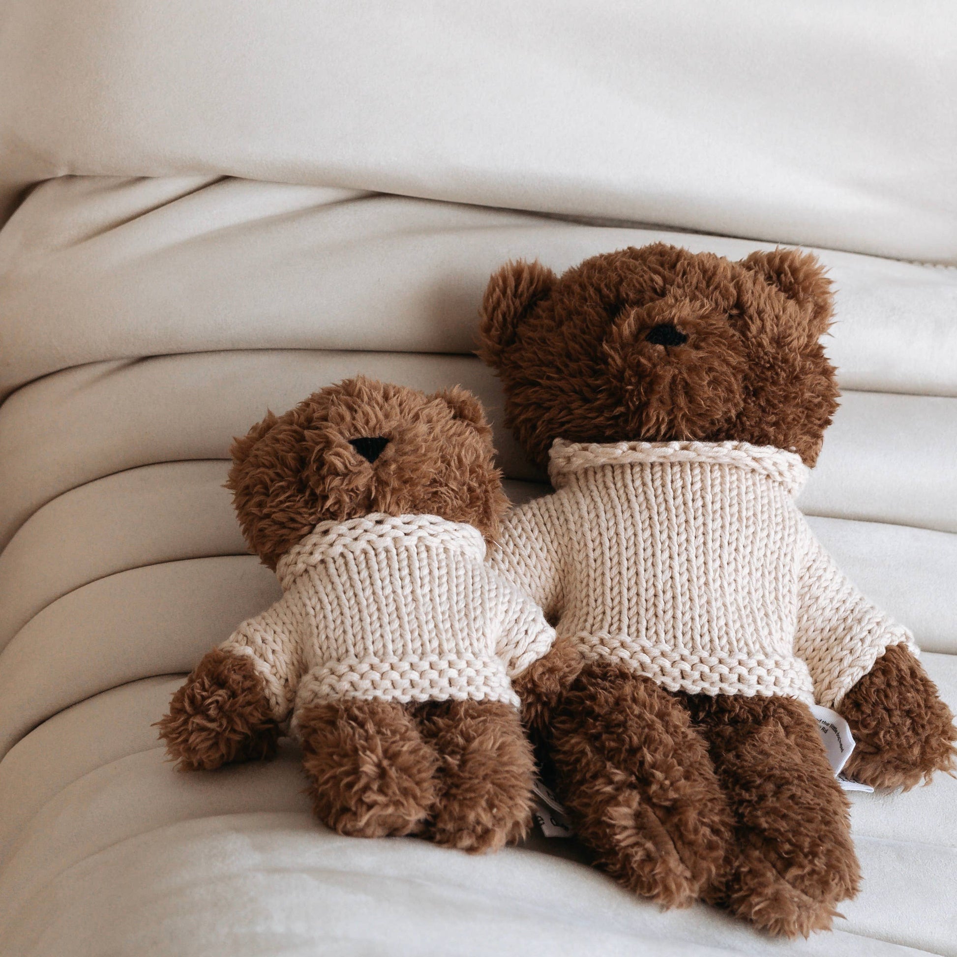 Two brown teddy bears wearing knitted sweaters sitting on a white surface.