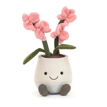 A plush toy representing a pink orchid with pale orange columns in a white pot with a smiling face and brown roots.
