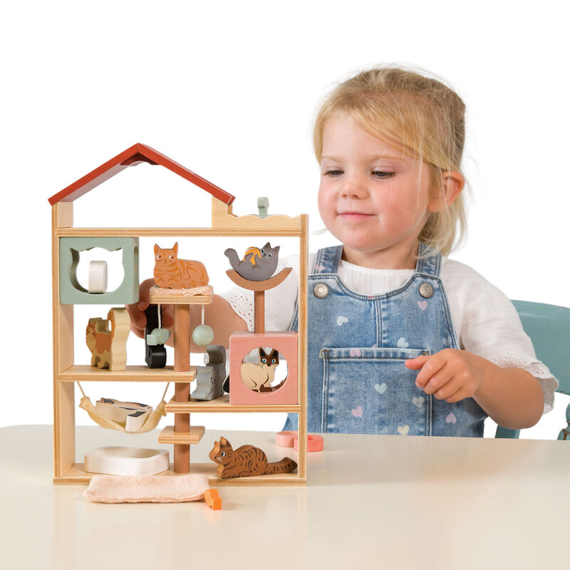 Child playing with a wooden toy house featuring kitten figures on a white background