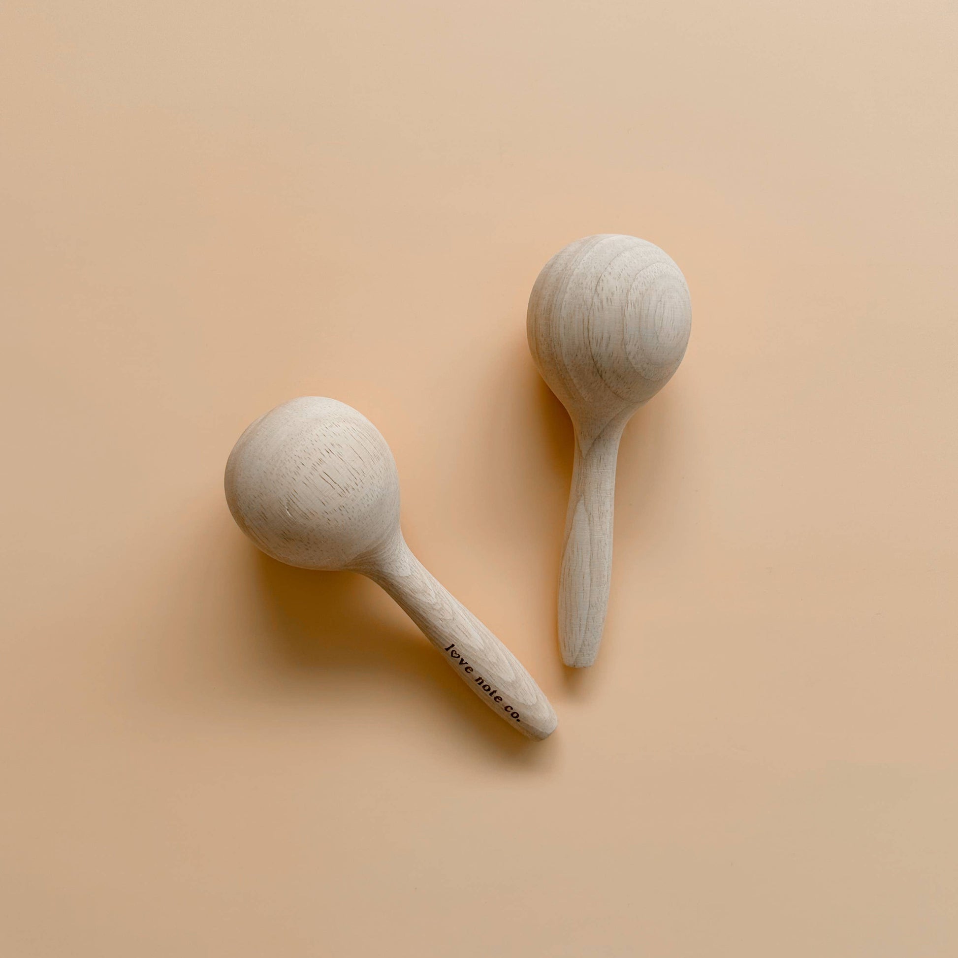 Pair of Love Note Co natural wooden maracas on a soft peach background.
