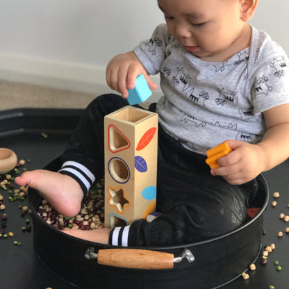 Child playing with shape sorter and colorful blocks in a black tray.