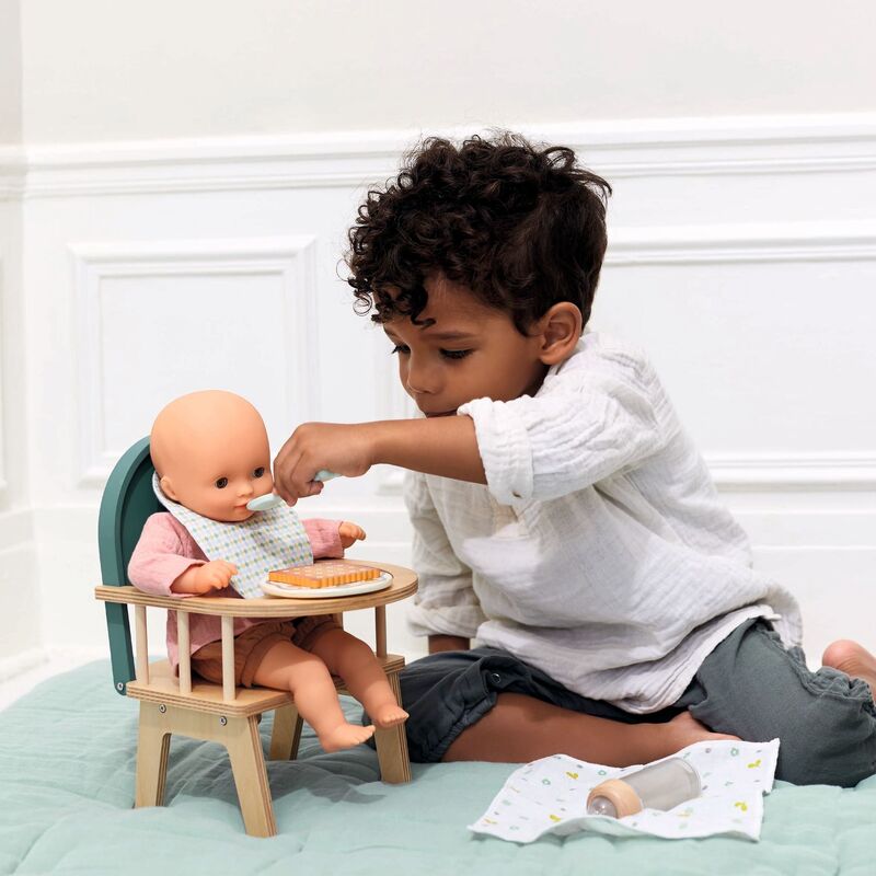 Young child feeding a play doll in a dolls wooden high chair