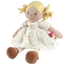 A doll with blonde hair, wearing a white linen dress with embroidered flowers and brown shoes.