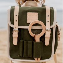 Green backpack with leather straps and a wooden ring on a blurred beach background
