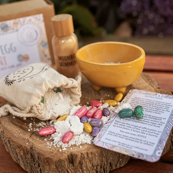 An Easter Egg Hunt Potion Kit displayed outdoors, including a cotton bag, a bottle with a liquid ingredient, a glass jar with powder, and a spell & affirmation card.