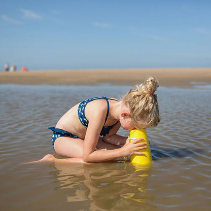 Child playing with a yellow Aquascope toy in shallow water near a beach