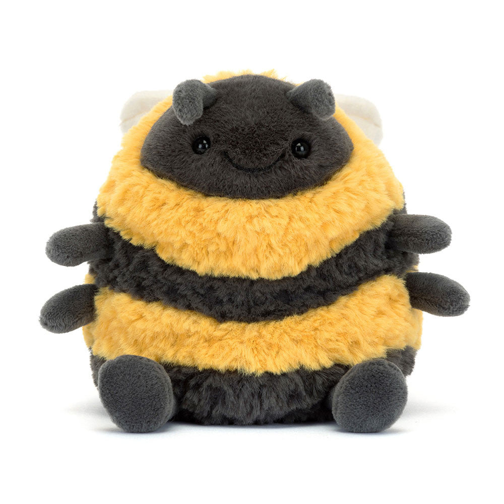 A plush toy made by Jellycat resembling a bumblebee with thick yellow and black striped fur, charcoal legs, a big stitched smile, and soft cream wings.