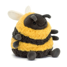 A plush toy resembling a bumblebee with thick yellow and black striped fur, charcoal legs, a big stitched smile, and soft cream wings.
