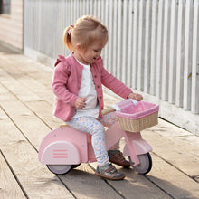Child on a pink scooter with a basket on a wooden deck