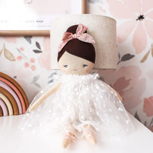 Stuffed doll with a white dress and pink bow in a decorative setting