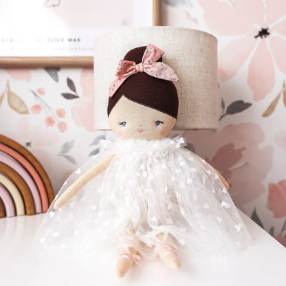 Stuffed doll with a white dress and pink bow in a decorative setting