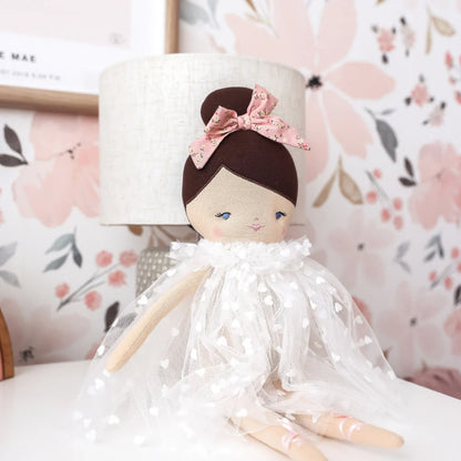 Handmade doll with a white dress and pink bow against a floral background