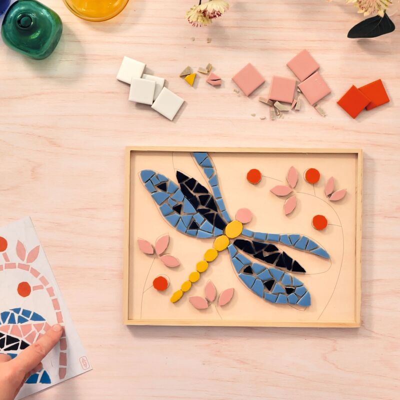 Colorful mosaic dragonfly on a wooden board with building blocks on a light wood surface