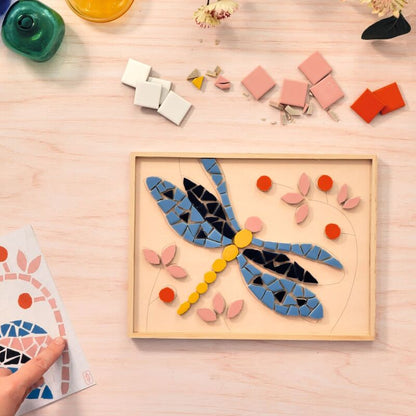 Colorful mosaic dragonfly on a wooden board with building blocks on a light wood surface