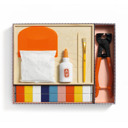 Set of art supplies including a bottle, brush, and other tools in an open box on a white background