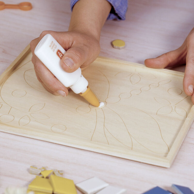 Person applying glue to a wooden puzzle piece with a bottle of glue.